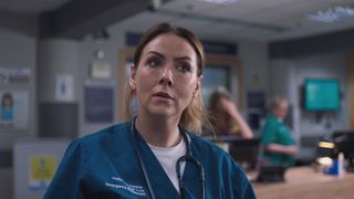 Stevie Nash at work wearing her blue uniform with her stethoscope around her neck looking tired and upset.