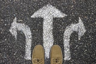 Two feet stood on road in front of white arrows pointing in different directions