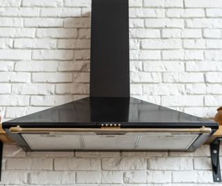A black range hood with clean filters on a white tile wall