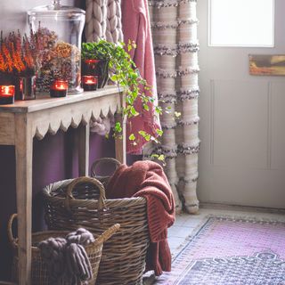 A hallway with a scalloped wooden console table and two wicker storage baskets underneath storing blankets and knits