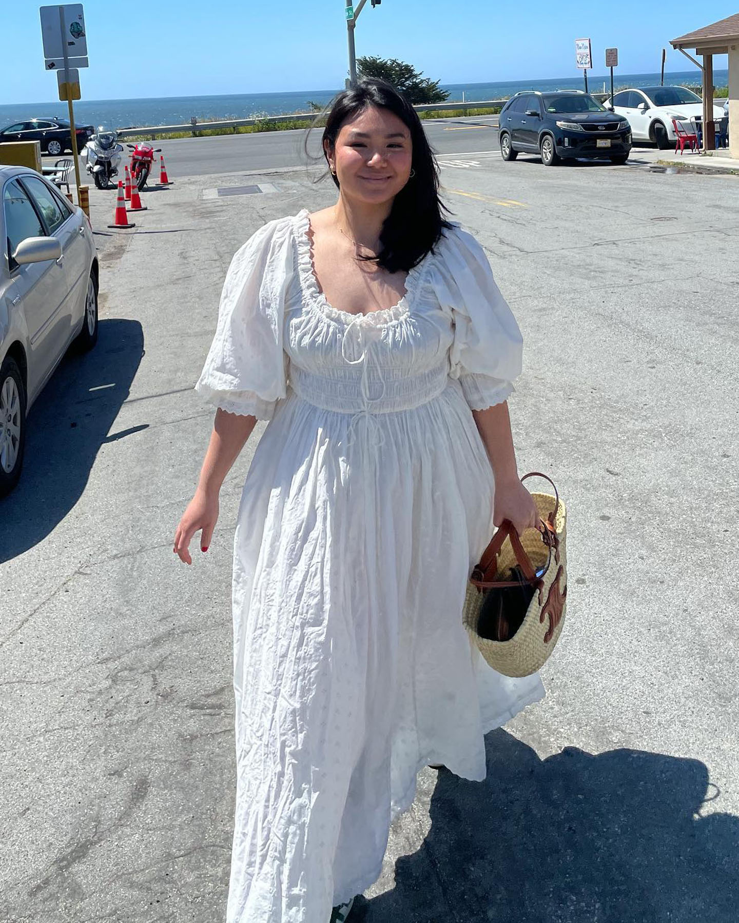 Mid-size fashion influencer Marina Torres walks on the streets of a beachside town wearing a puff-sleeve white dress.