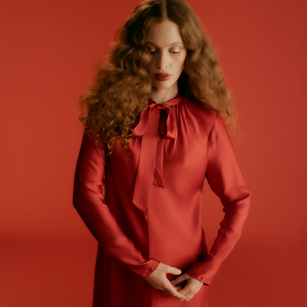Model wearing a red satin Ghost dress with tie up collar infront of a red background