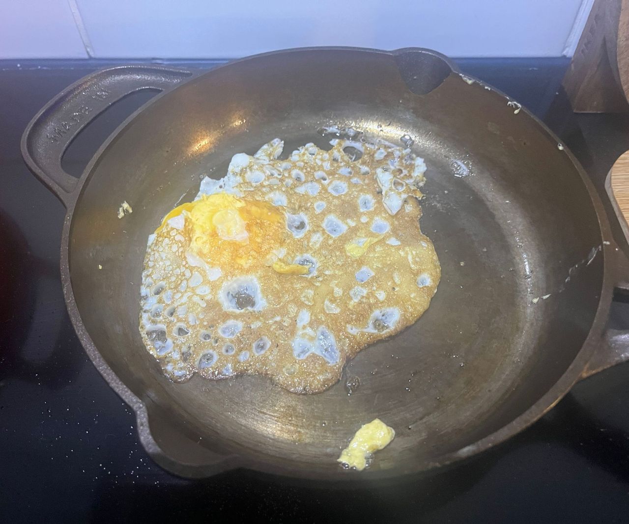 A small bronze colored cast-iron skillet on a black glass stove with an upside down fried egg inside.