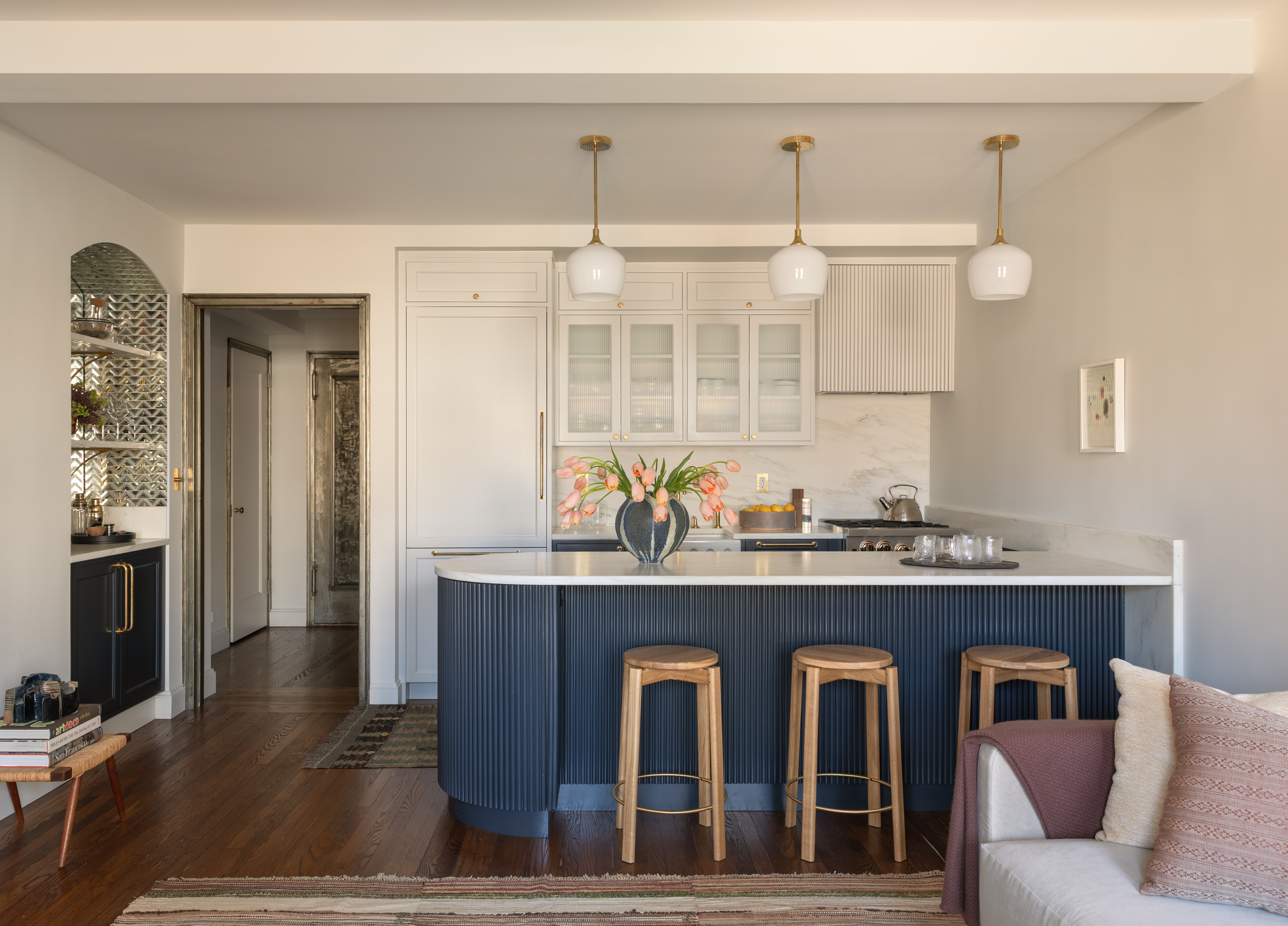 A kitchen with a blue island, white pendant lights and wooden flooring