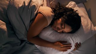 Woman asleep on her side, hugging a pillow