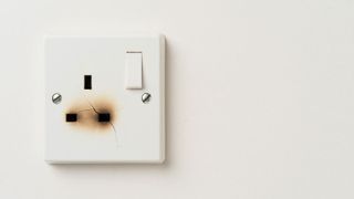 Single white plug socket with burn marks on bottom pins against a white wall