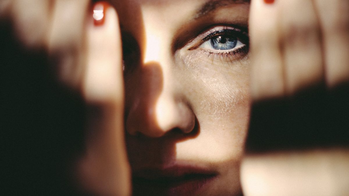 A woman holding her hands up in front of her face in moody lighting