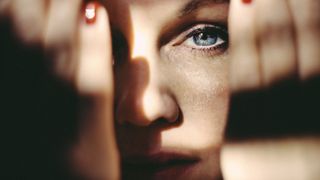 A woman holding her hands up in front of her face in moody lighting