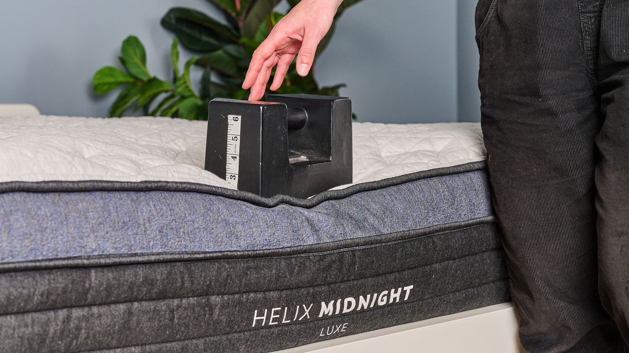 The image shows a weight placed on the edge of a white mattress with a navy blue trim