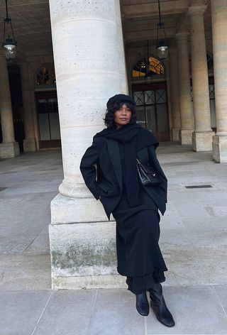 Woman wearing an all-black outfit with a black scarf.