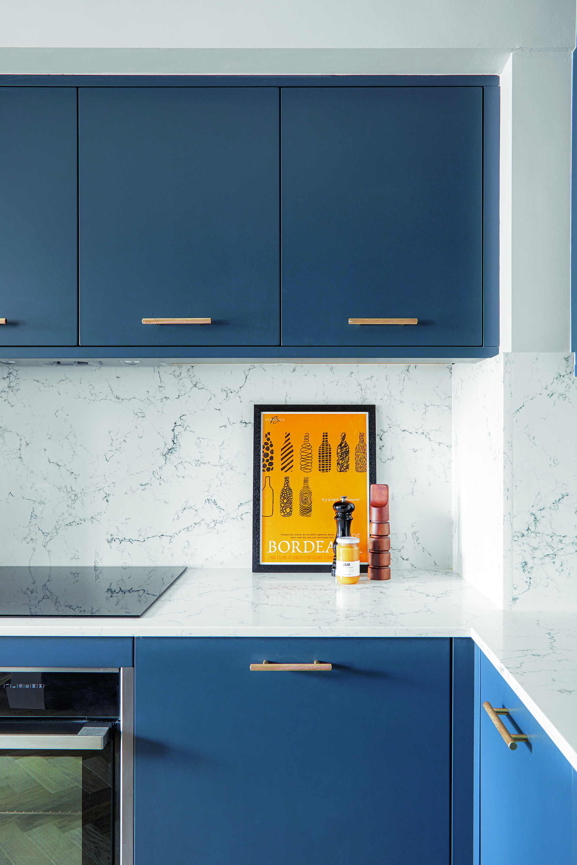 A small kitchen area with bright blue cabinets with slim gold coloured handles, and marbled tiled walls and worktops