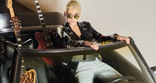 Carmen Vandenberg sits in an open-top convertible with guitars in the back