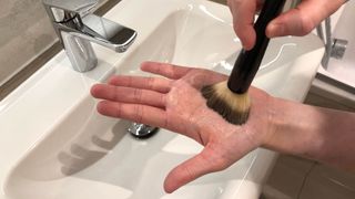 Soap being applied to a makeup brush using the palm of the hand