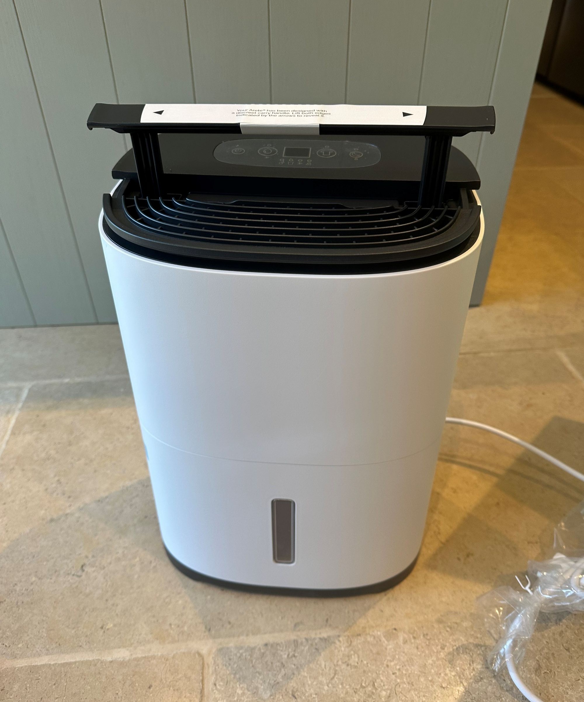 A dehumidifier with the handle lifted up on limestone tiles