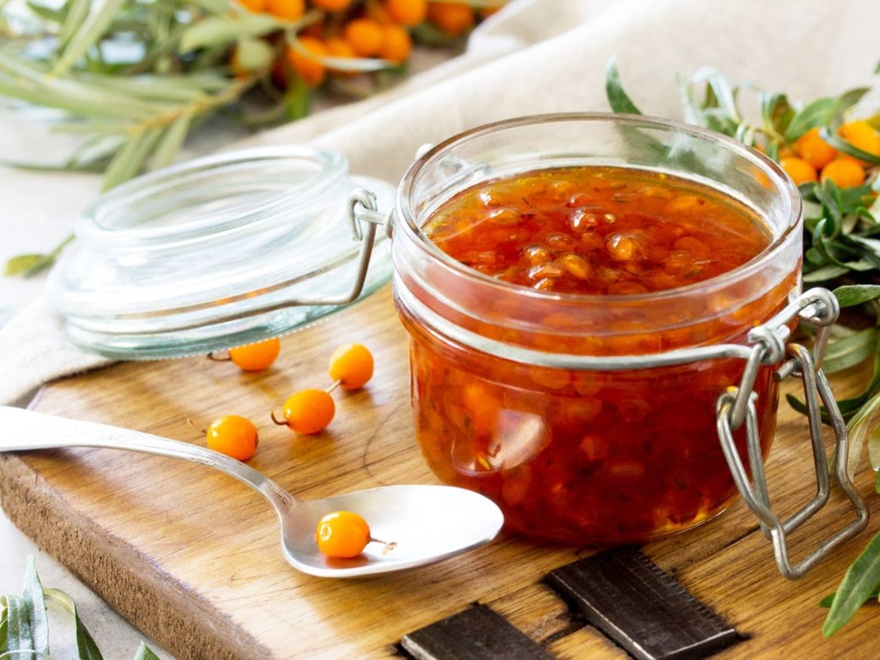 An open jar of sea buckthorn jam next to several whole sea buckthorn berries