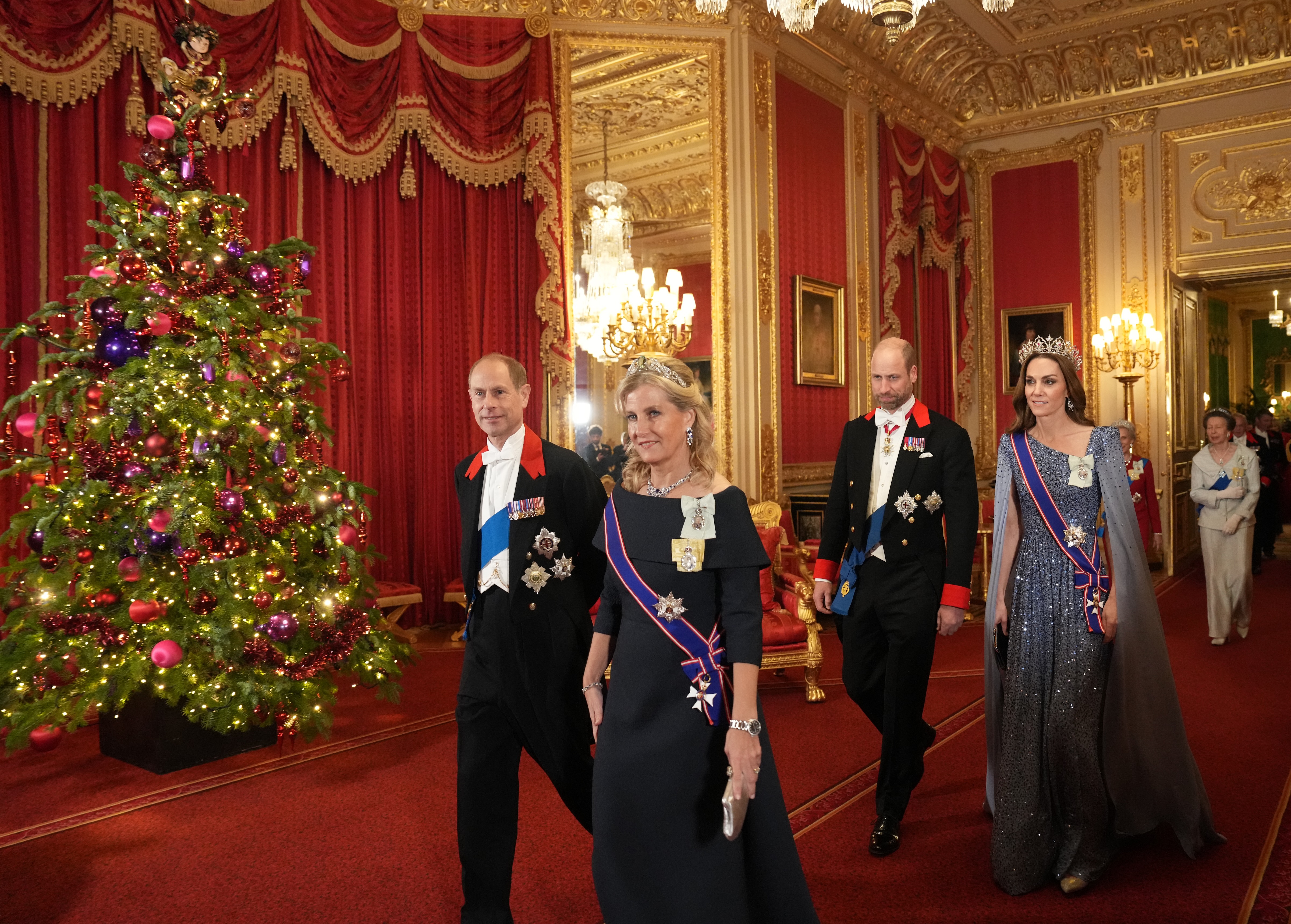 Prince Edward, Duchess Sophie, Prince William and Princess Kate walking past a Christmas tree in suits, tiaras and evening gowns