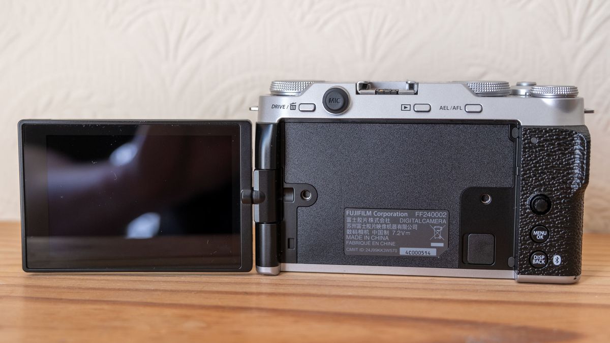 The Fujifilm X-M5 with screen flipped out to the left on a wooden shelf.