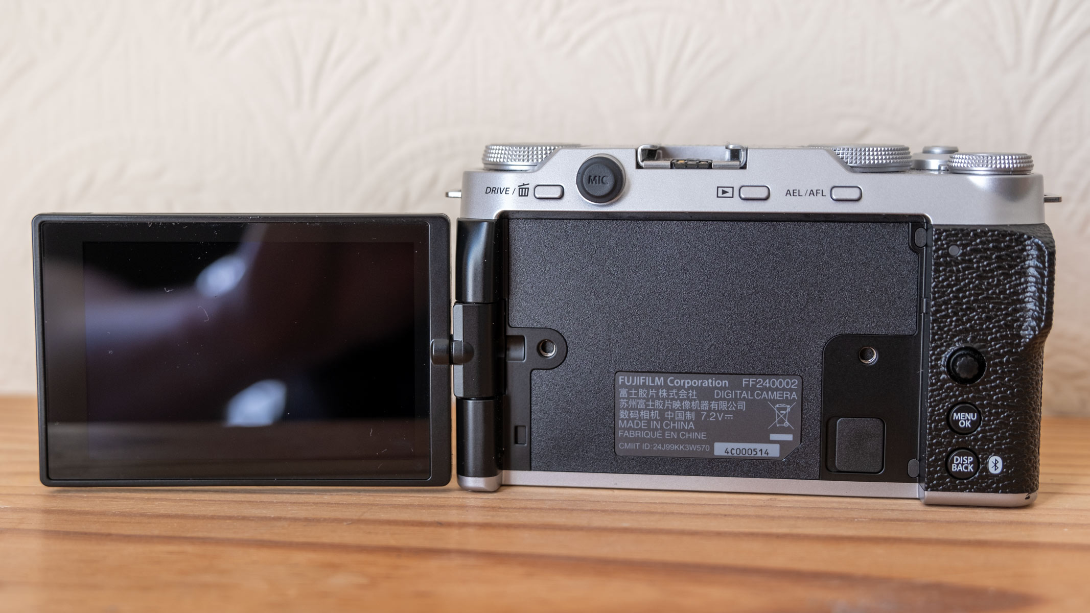 The Fujifilm X-M5 with screen flipped out to the left on a wooden shelf.
