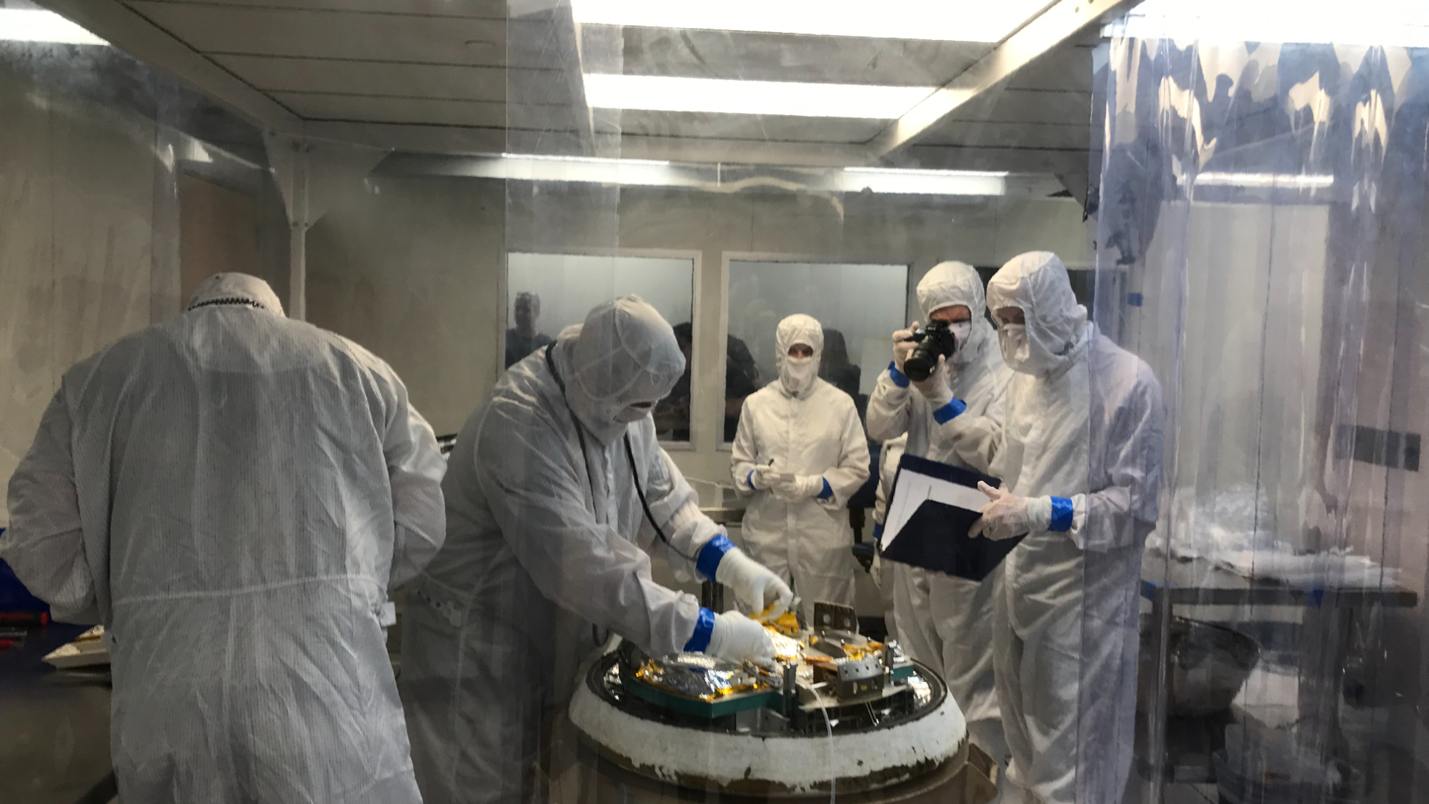 technicians in a clean room examine a mock space capsule