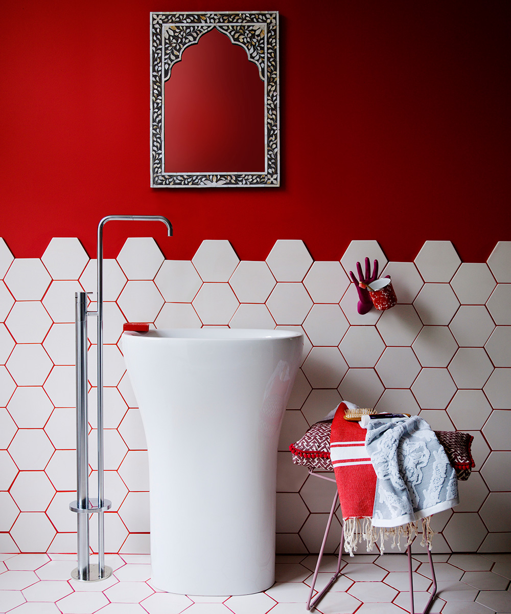 An example of bathroom paint ideas showing a red wall with white hexagonal tiles half way up with wall and a white sink