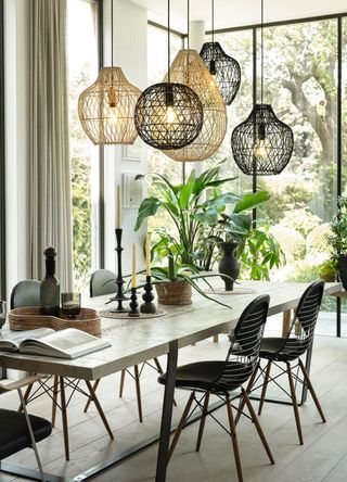 Dining room with floor to ceiling glass windows with art-like rattan lighting above a wooden dining table