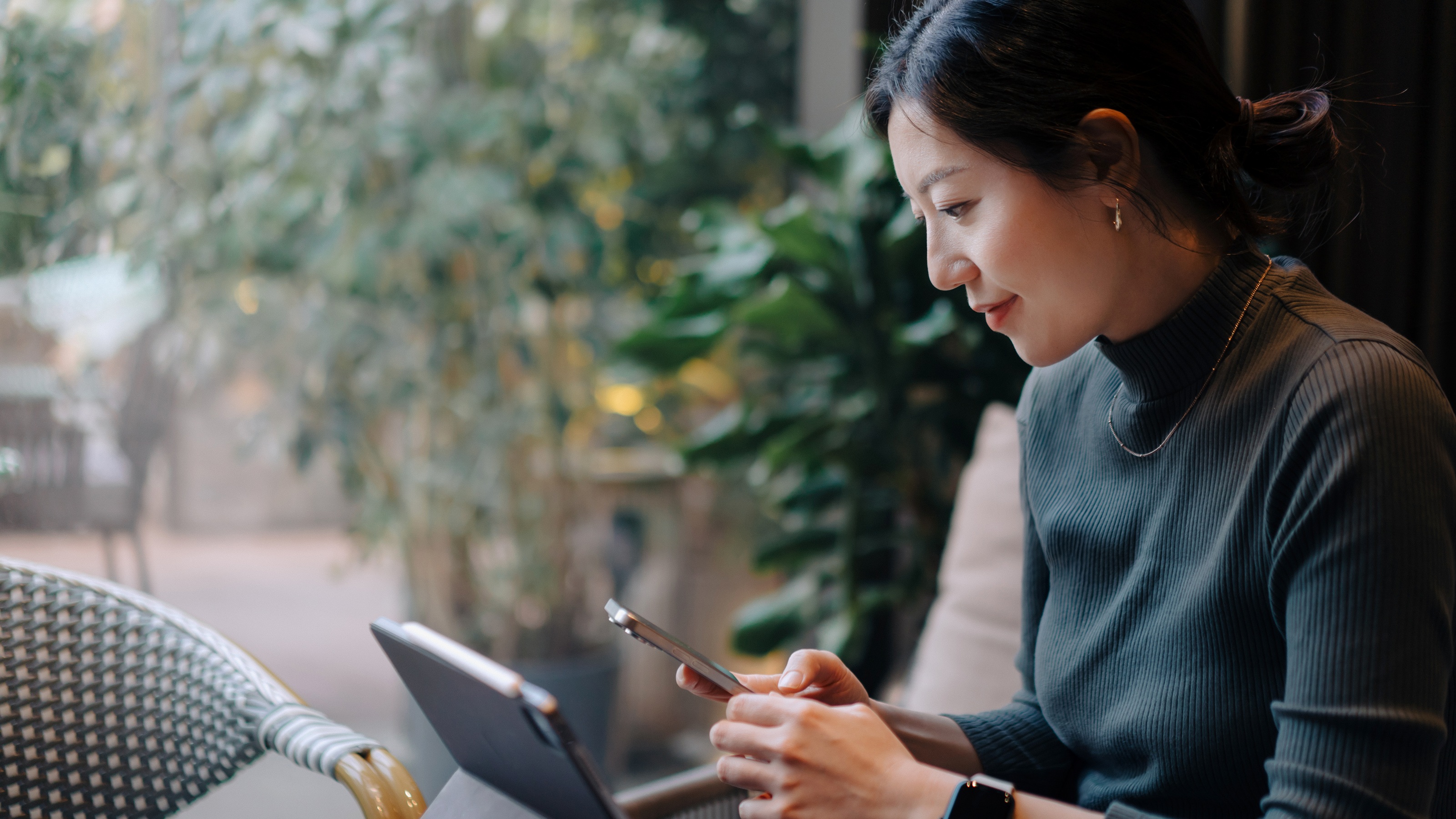 A woman smiles as she looks at her phone while sitting at her desk. 