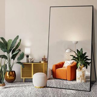 Gogexx Oversized Black Alloy Mirror with a black frame leaning against a wall in a bedorom with plants, rug and orange chair