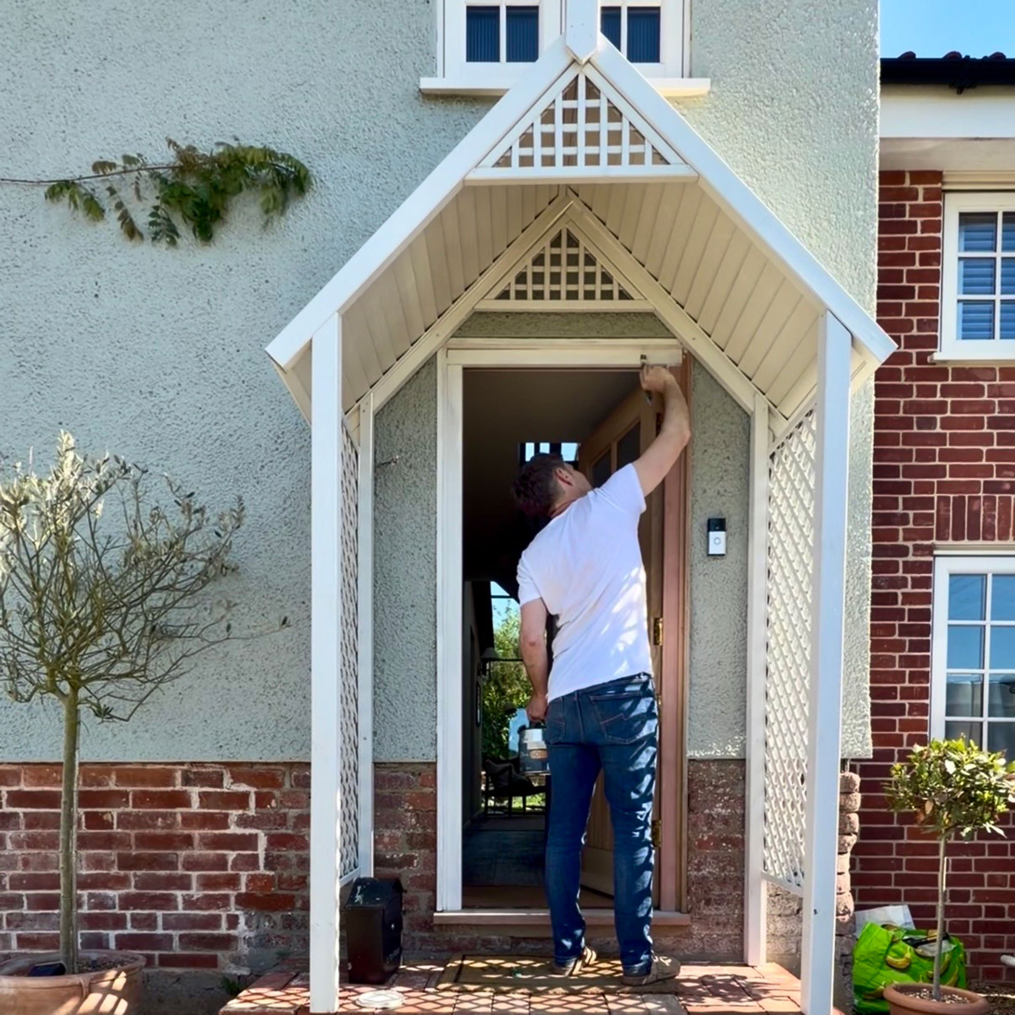 Man painting trim of front door of country cottage underneath cream coloured porch
