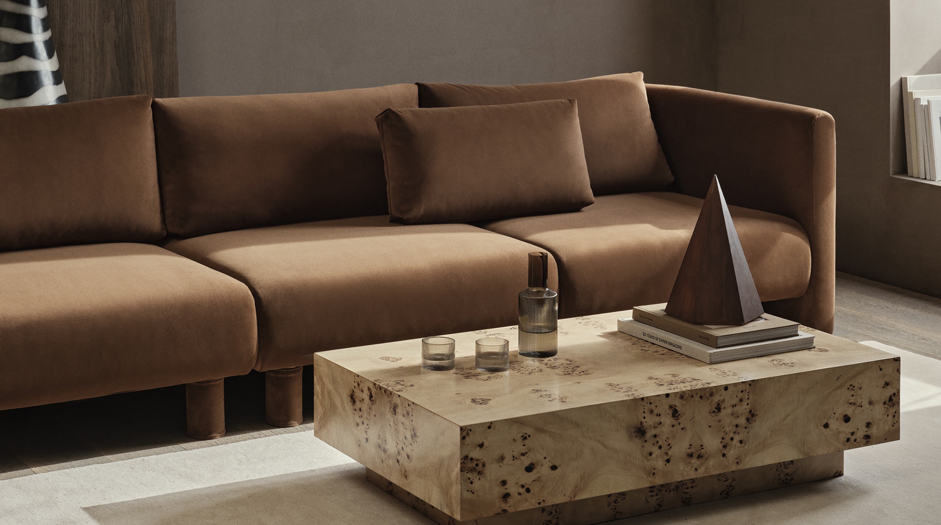 a burl coffee table in front of a rust color sofa