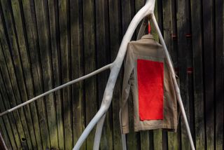Brown jacket with red back by Folk x Architectural Association hanging on wood outdoors