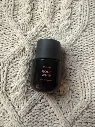 Phlur rose whip bottle on a grey weave blanket