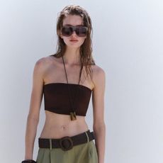 Zara model wearing pleated belt short, brown tube top, and oversized sunglasses. 