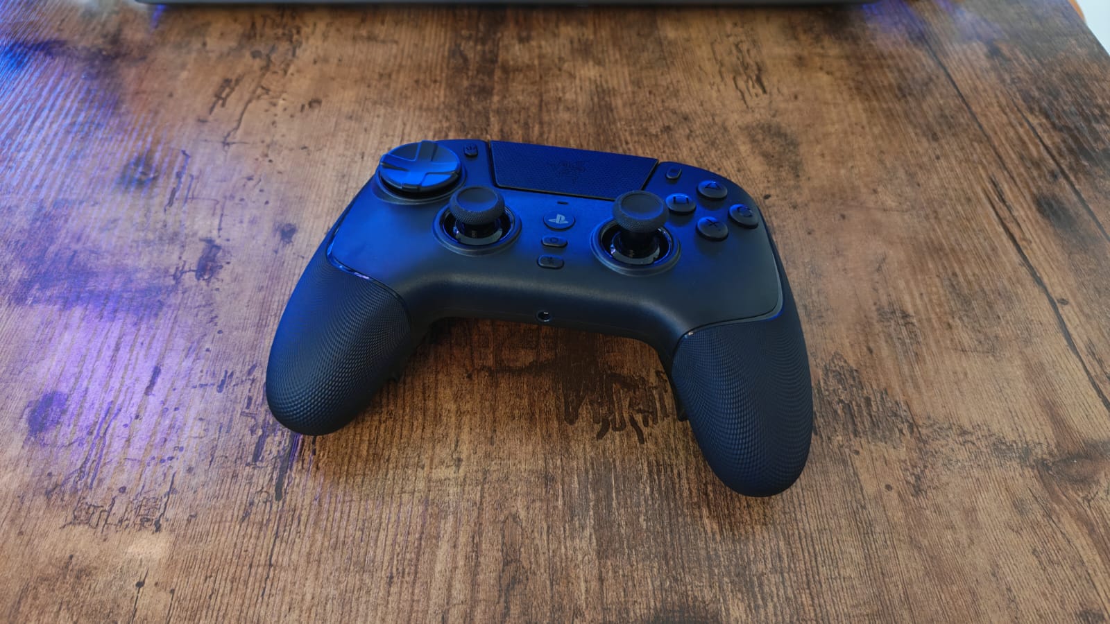 The black Razer Raiju V3 Pro lying on a wooden desk under blue lighting
