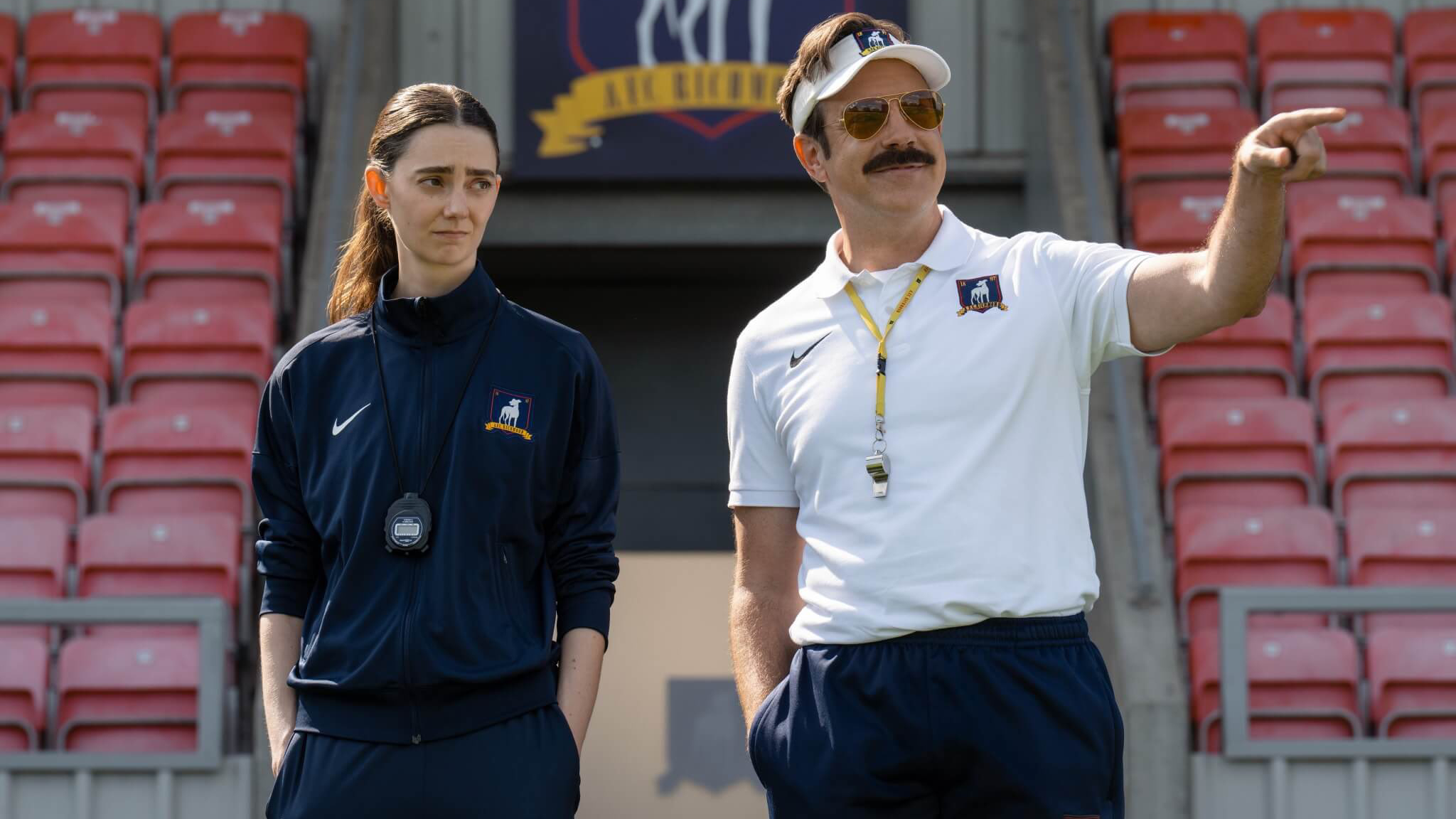 L-R: Jason Sudeikis and Tanya Reynolds in front of the AFC Richmond stands in a first-look still for "Ted Lasso" season 4