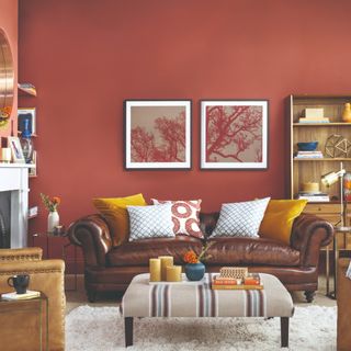 A living room painted in a red terracotta shade with a brown leather sofa and a fireplace