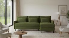 Image of a dark green sofa in a neutral living room. There are three other beige chairs around the sofa and a beige rug on the ground.