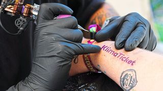 Closeup of a person getting the Klimaticket logo tattooed onto their arm