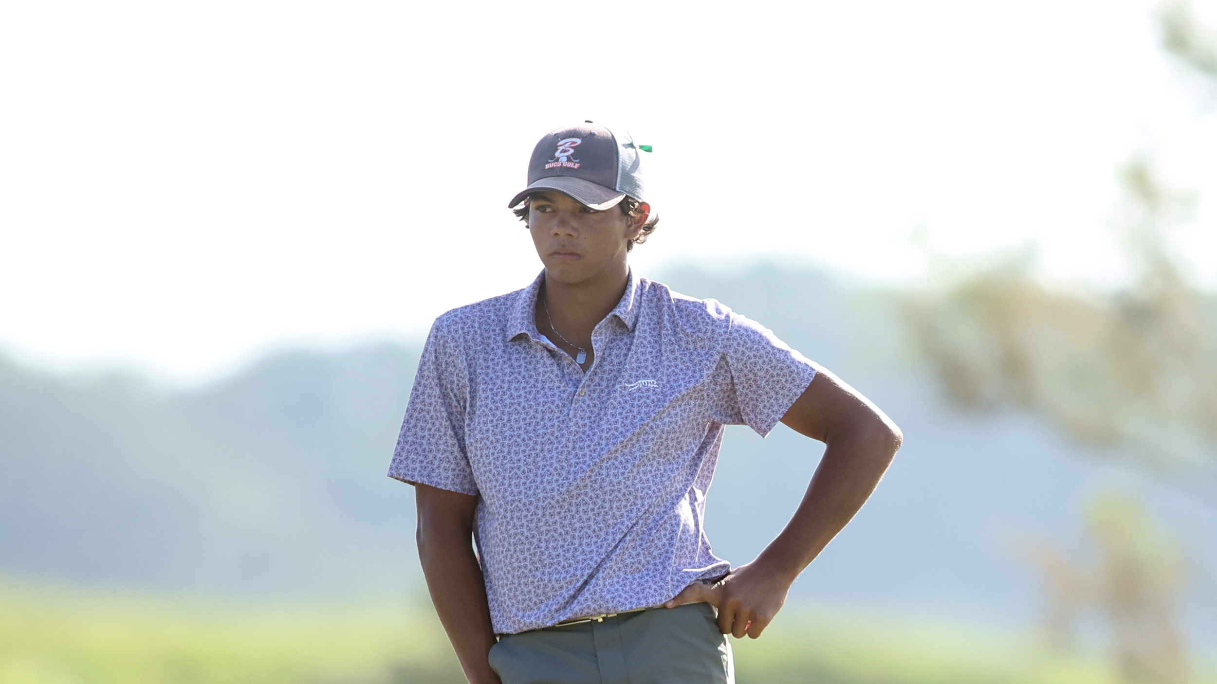 Charlie Woods stands with a hand on one hip and wearing a glum expression during the 2025 US Junior Amateur second round