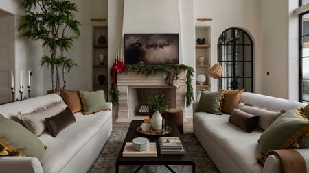 bright living room with two white sofas facing a stone fireplace decorated with evergreen garland, red ribbons, and a painting of Santa and his sleigh