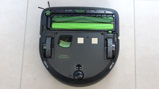 En iRobot Roomba S9+ vendt på hovedet og ligger på et klinkegulv