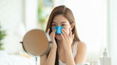 young women applying a grease-removing cloth to her nose while looking in a small mirror