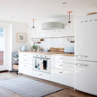 kitchen with wooden flooring, white walls tiles, cabinets and white Smeg fridge