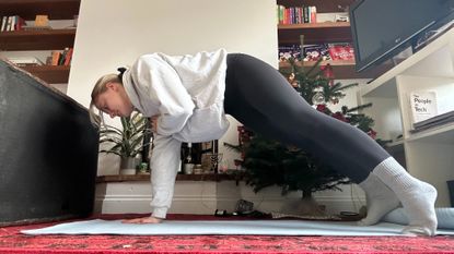 Woman doing plank shoulder taps in living room.
