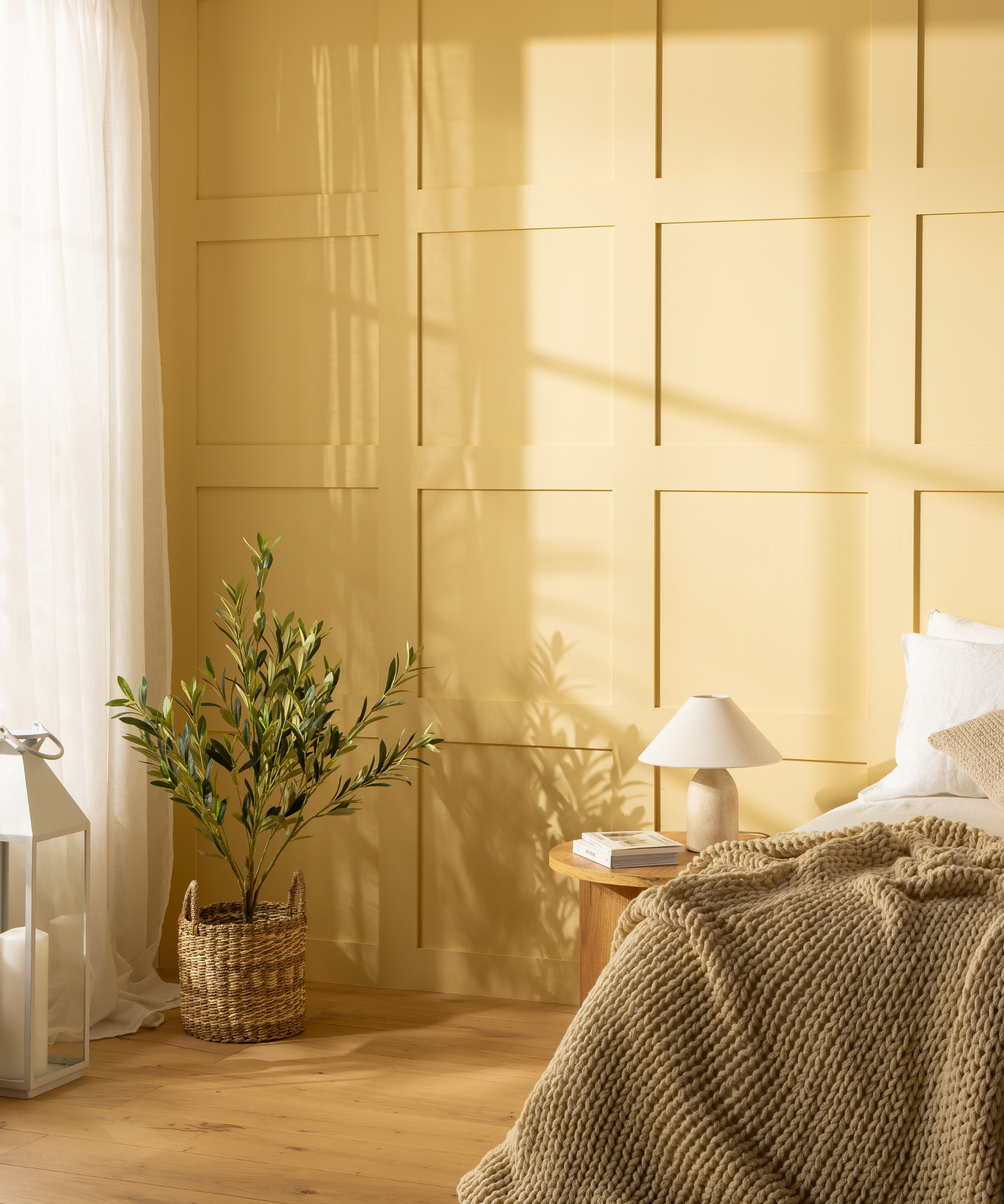 Yellow shaker panelled wall behind a bed, side table and plant