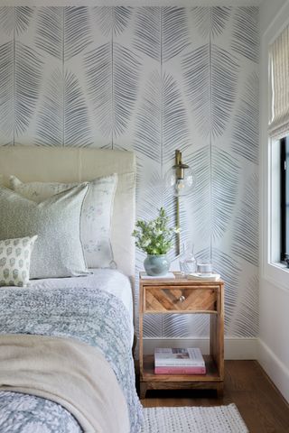 bedroom with leafy wallpaper and patterned bedding wood bedside table