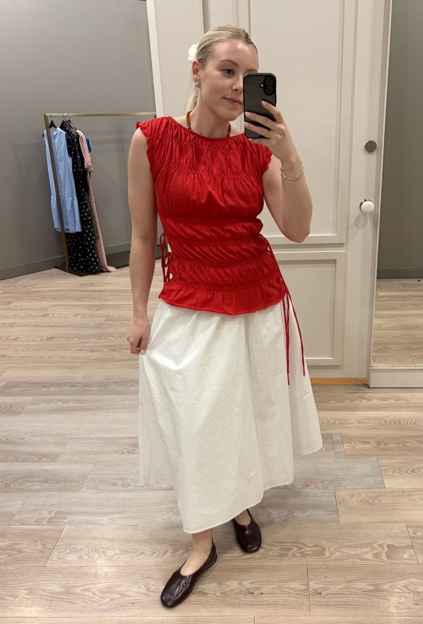 Woman wears red top, white skirt and burgundy ballet flats