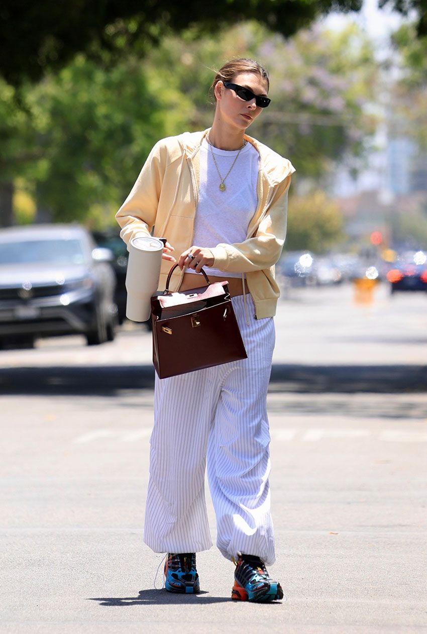 Vittoria Ceretti wearing a yellow zip-up hoodie, white cropped t-shirt, striped pants, and colorful sneakers.