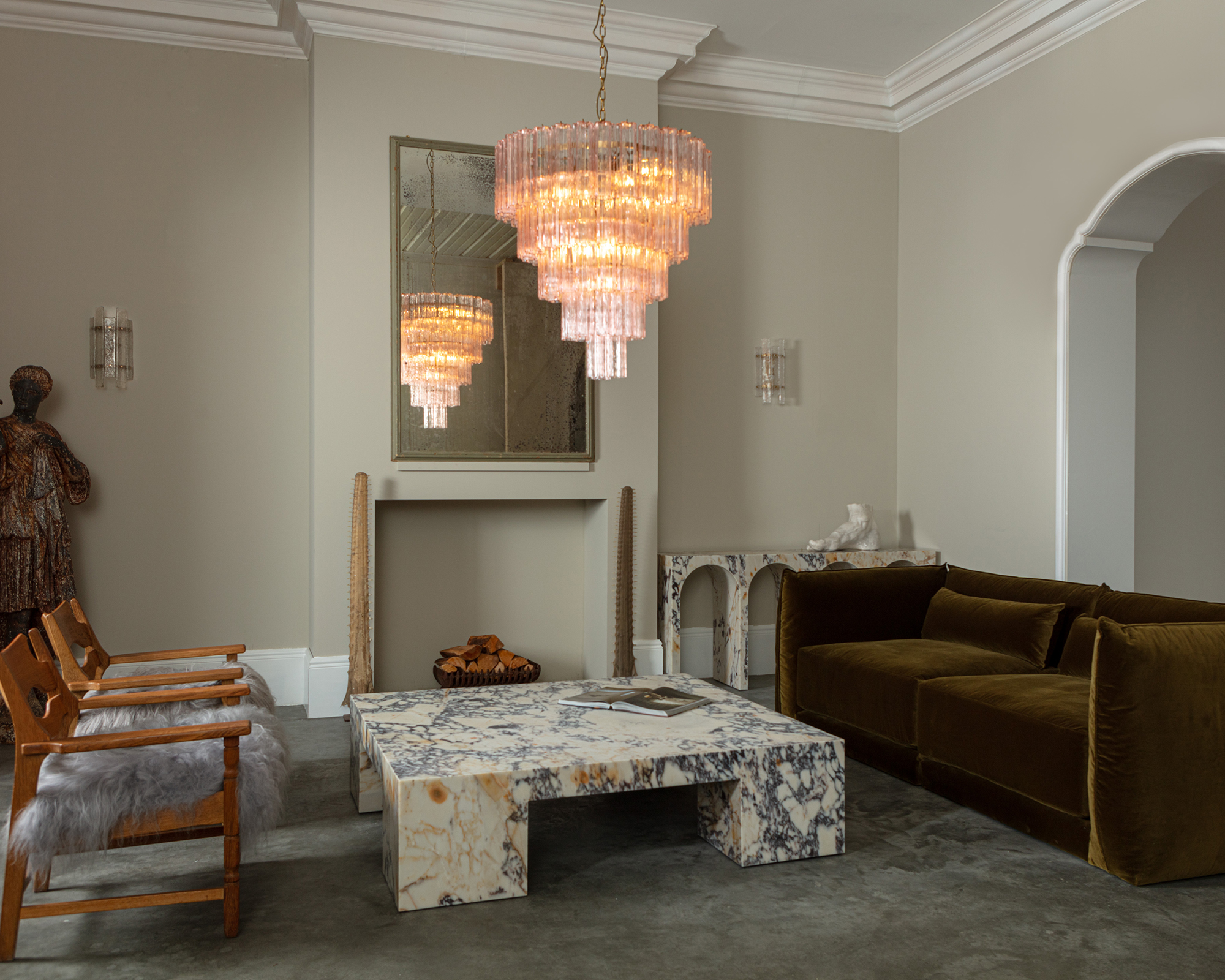 marble coffee table in the middle of a large living room with a glass chandelier hanging above it