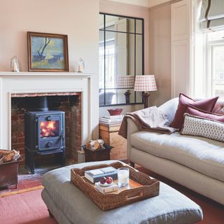 Pale coloured sofa in small cottage sitting room with upholstered footstool, terracotta rug and woodburning stove in fireplace