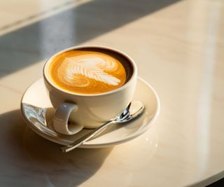 A latte in a wide coffee mug on a cream stone table